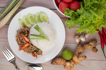 Stir fried pork with basil, fried egg in a white dish .