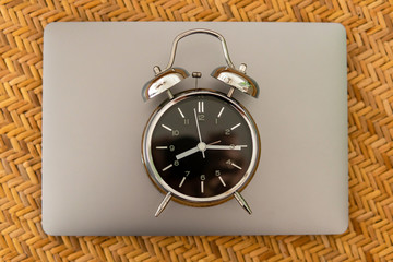 Alarm clock on laptop on braided texture. Online working concept.