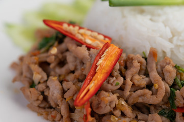 Stir fried pork with basil, fried egg in a white dish .