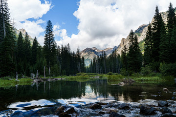 Grand mountains Grand Tetons in Wyoming. Mountain landscape with spring waters and mountain lakes. Blue sky. White clouds. Deep forest woods. 