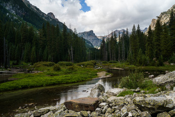 Grand mountains Grand Tetons in Wyoming. Mountain landscape with spring waters and mountain lakes. Blue sky. White clouds. Deep forest woods. 