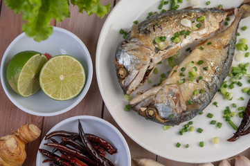 Two cooked mackerel, placed in a white dish, sprinkled with spring onions.