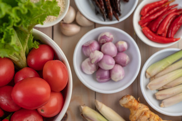 Red onions, lemon, lemongrass, chilies, garlic, galangal, and lettuce in a cup on a wooden floor.