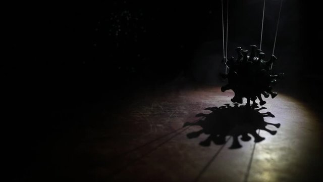 Creative concept of manipulation with coronavirus. Crowd looking on big Corona virus miniature. The hand controls the Covid19 miniature with strings on a dark foggy background. Selective focus