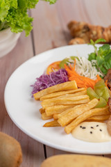 Fish steak with french fries, kiwi, lettuce, carrots, tomatoes, and cabbage in a white dish.