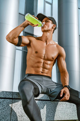 Resting time. Tired sporty man resting after training. Photo of fitness model with bottle of water, sitting outdoor. Sports and healthy life
