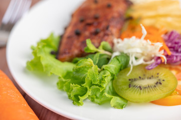 Fish steak with french fries, kiwi, lettuce, carrots, tomatoes, and cabbage in a white dish.