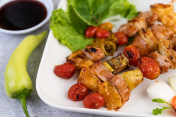 BBQ with a variety of meats, complete with tomatoes and bell peppers on a white plate.