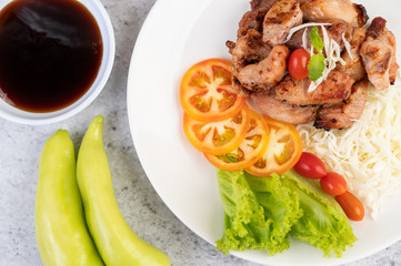 Grilled pork cutlet with tomatoes and salad, arranged in a white dish.
