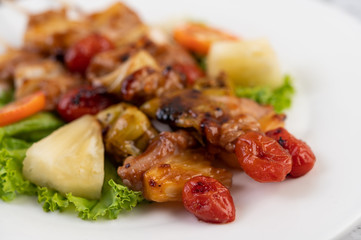 BBQ with a variety of meats, complete with tomatoes and bell peppers on a white plate.