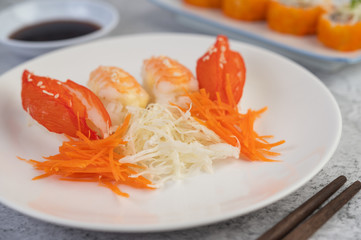 Sushi is in a plate with chopsticks and dipping sauce on a white cement floor.