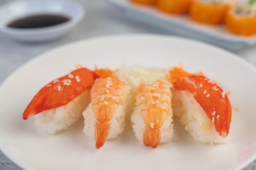 Sushi is on a plate with dipping sauce on a white cement floor.