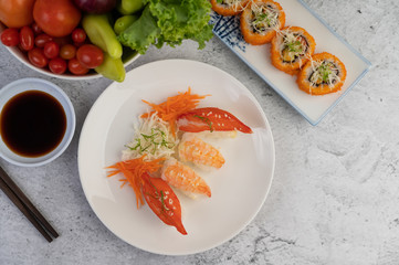 Sushi is in a plate with chopsticks and dipping sauce on a white cement floor.