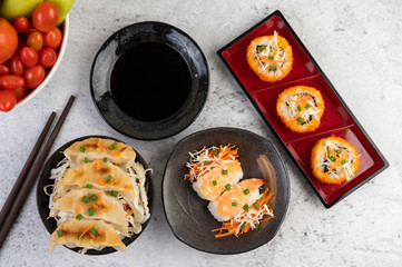 Sushi is in a plate with chopsticks and dipping sauce on a white cement floor.