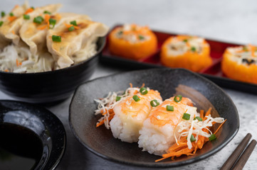 Sushi is in a plate with chopsticks and dipping sauce on a white cement floor.