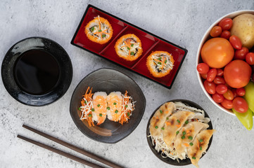 Sushi is in a plate with chopsticks and dipping sauce on a white cement floor.