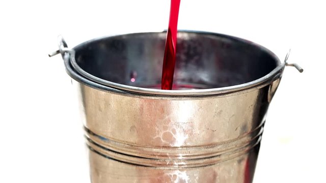 The red liquid is poured into a steel bucket, isolated on white background, slow motion.