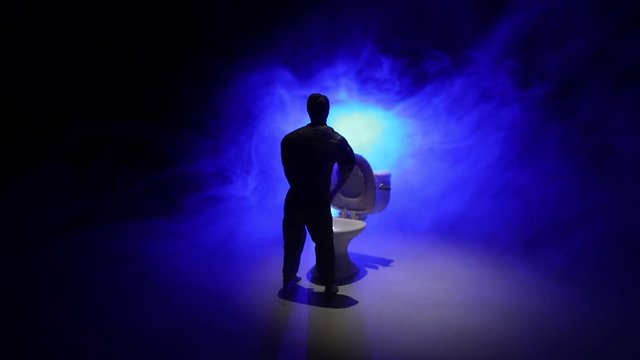 Creative concept. Miniature white toilet bowl on dark foggy background. Man peeing. Selective focus