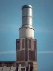 A closeup of a stainless steel round or cylinder shaped smokestack chimney or vent on top of a limestone clad masonry building in Chicago.