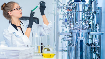 The girl examines the substance in a test tube against the background of a laboratory bioreactor....