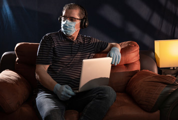 Middle aged man working at home on his computer for the coronavirus using protective equipment such as gloves and mask