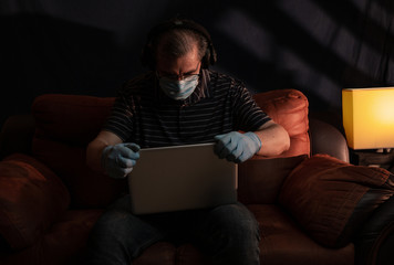 Middle aged man working at home on his computer for the coronavirus using protective equipment such as gloves and mask