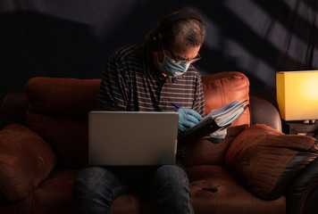 Middle aged man working at home on his computer for the coronavirus using protective equipment such as gloves and mask