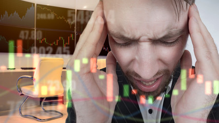 A man has a headache because of too much stock information. Hard work. Trading on the stock exchange requires concentration. A man holds his head with his hands against the background of stock data.