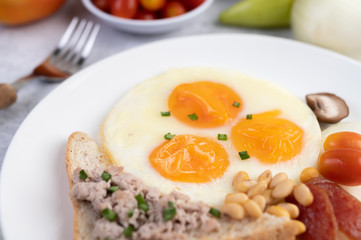 Breakfast consists of fried eggs, sausage, minced pork, bread, red beans and soy on a white plate.