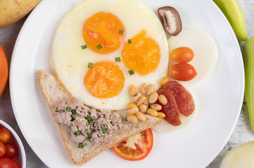 Fototapeta na wymiar Breakfast consists of fried eggs, sausage, minced pork, bread, red beans and soy on a white plate.
