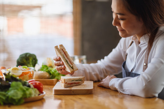 Closeup image of a beautiful female chef cooking and eating a whole wheat sandwich in kitchen
