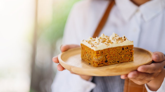 A waitress holding and serving a piece of homemade carrot cake in wooden tray