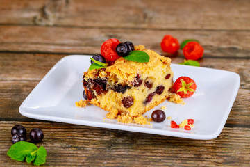 Piece of blueberry coffee cake on white plate on wooden background.