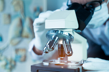 Doctor or scientist wear medical face mask and looking in microscope while working on medical research in science laboratory