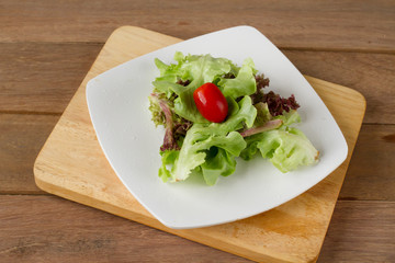 Red ripe tomato put with green leaf of Oak on white plate and wooden table.