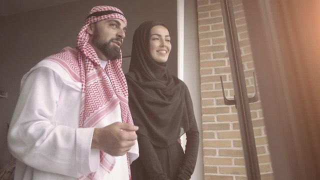 Arab couple looking throught window at home.