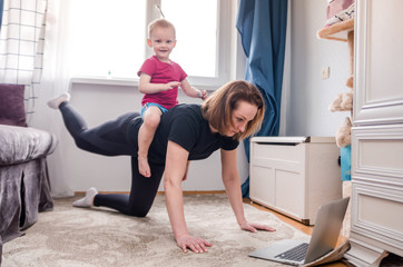Beautiful young woman in a black tracksuit doing workout exercises at home watching videos on her...