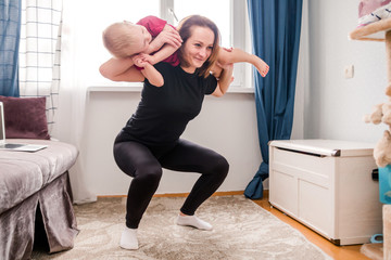 young sportive mother carrying her little child on shoulders while doing squats