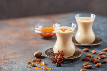 Golden Cinnamon Saffron Almonds Milk. Golden milk with species cardamom, turmeric, cinnamon, honey and ginger on wooden background. Trendy hot Healthy Vegan Drink. Indian Garam Badami Doodh.