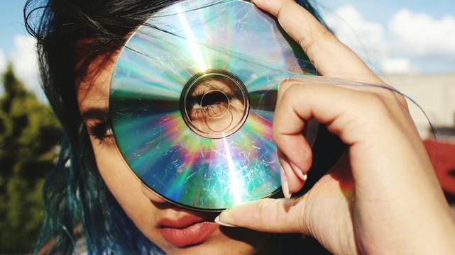 Young Woman Looking Through Hole Of Compact Disk