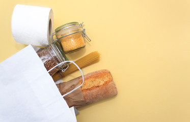 Donation food. Corn grits, buckwheat in jar, spaghetti, bread, toilet paper in white bag on yellow background.