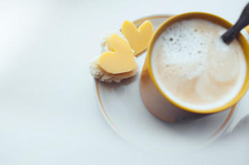 romantic homemade simple Breakfast sandwiches in the shape of a heart with cheese and a yellow mug with milk foam on the window.