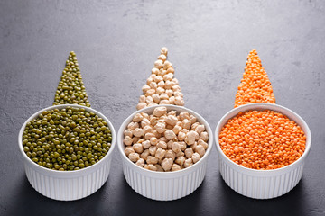 Three cups of legumes on dark background - mung beans, chickpea and red lentil. Horizontal...