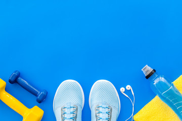 Fototapeta na wymiar Fitness equipment. Sneakers, dumbbells, headphones on blue background top view copy space
