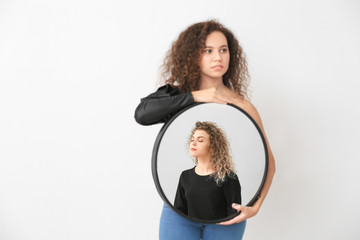 Fototapeta na wymiar Beautiful model holding mirror with reflection of young woman on white background