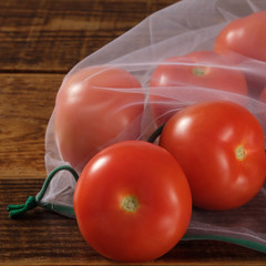 Zero waste, plastic free recycled textile produce bag for carrying fruit tomatos or vegetables, a wooden surface. Reusable using.