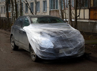 A wrecked car wrapped in plastic wrap in the yard of a house