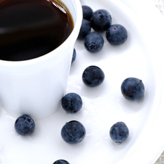 cup of black coffee with blueberries on white plate