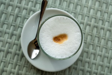 Glass with latte coffee on a saucer with a spoon. A table in a street cafe. White borders of milk and brown edges of coffee are visible in a glass. Clear day. The city of Tbilisi, Georgia.