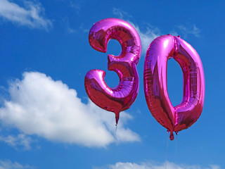 pink helium balloons on blue cloudy sky, celebrating the age thirty with number balloons, birthday background